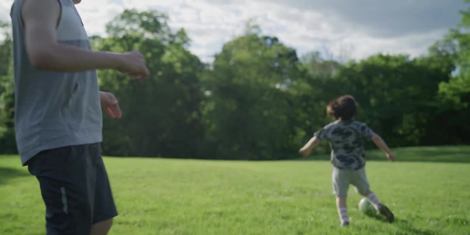 A little boy runs by and kicks a soccer ball while an older boy limps by struggling to kick the ball