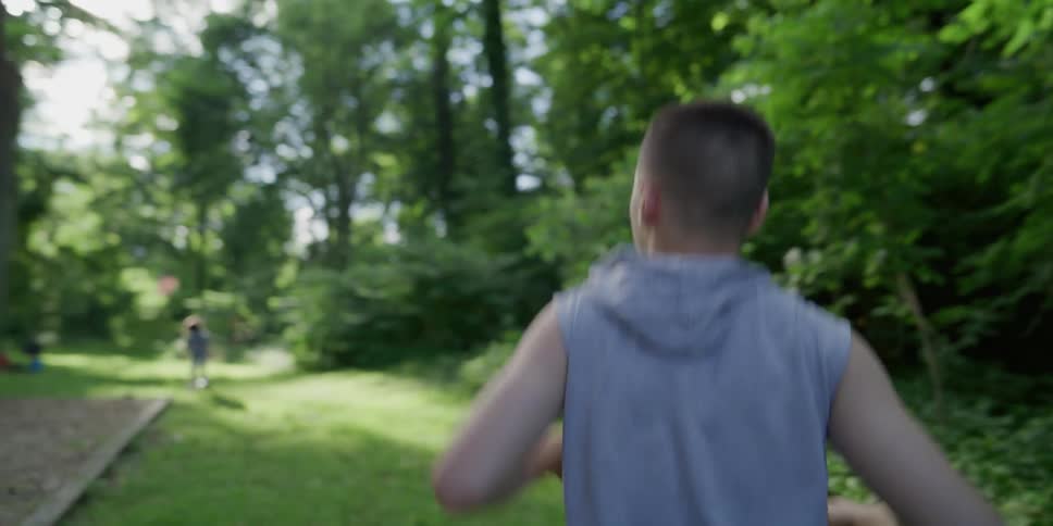 A disabled boy walks towards his friend in a park