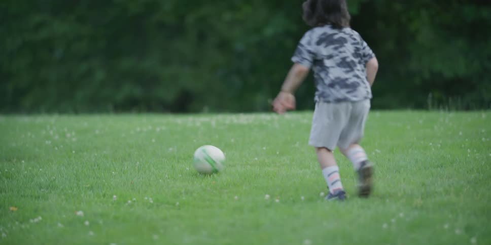 A young boy is kicking a soccer ball around on the lawn