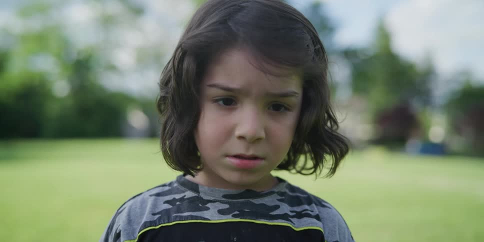 A boy stands outside looking at the camera as he moves his arms
