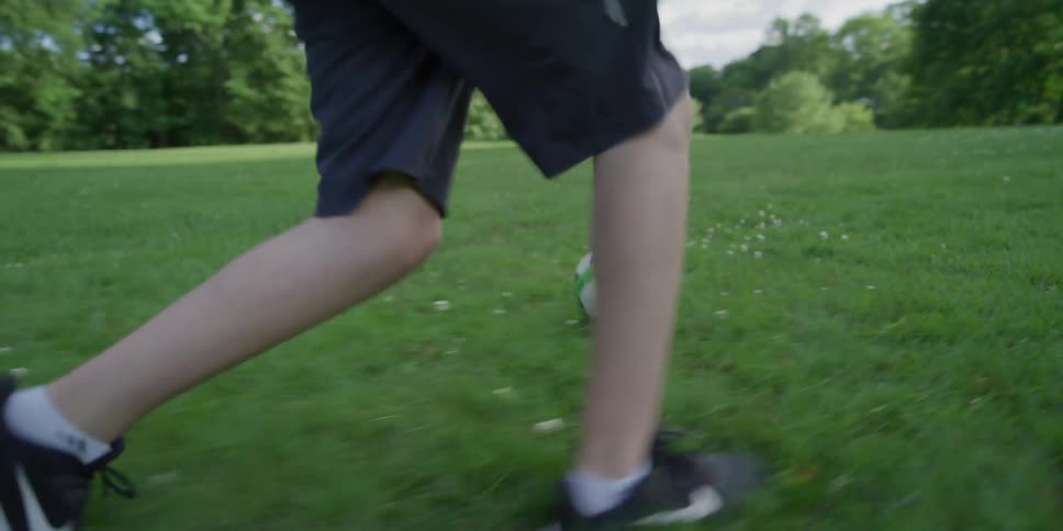 A disabled boy kicks a ball in a park with his friend