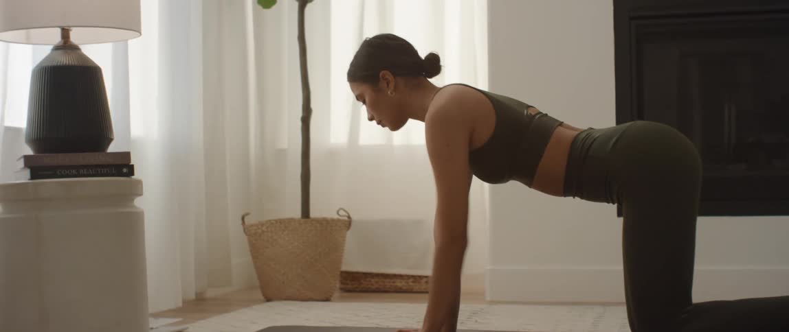 Woman on her hands and knees on a yoga mat in a living room doing yoga poses