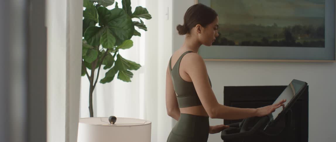 A young woman programs exercise equipment before her workout at home