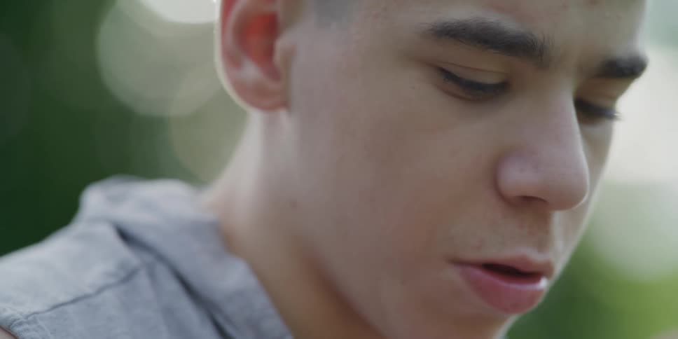 A boy leans in and talks to his brother who is playing on a phone