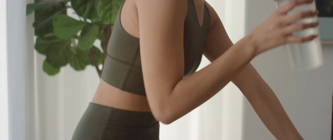 A woman on a spin bike at home takes a drink of water