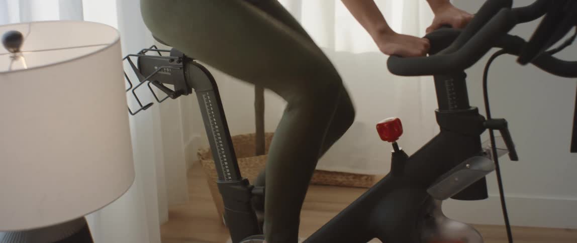 A young woman in athletic wear adjusts a knob on an exercise bike as she pedals