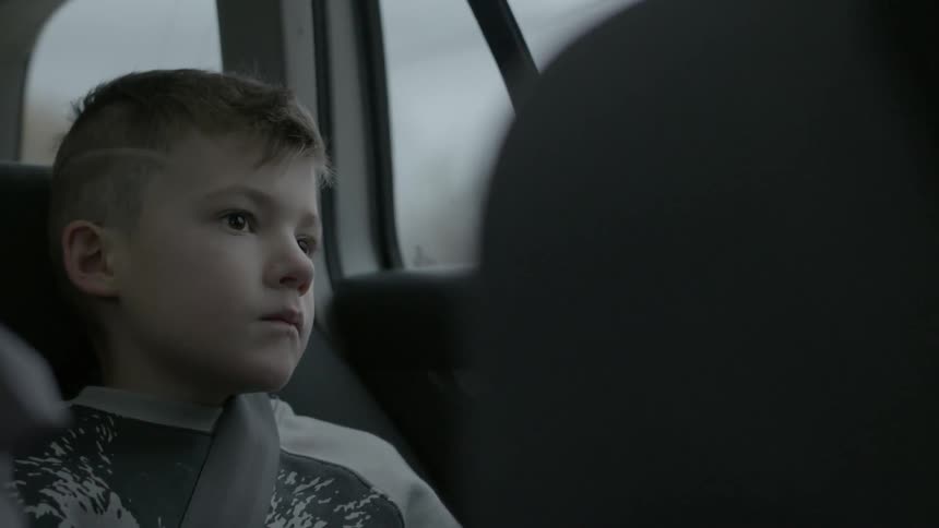 A boy is sitting with a seat belt on in back of a moving car