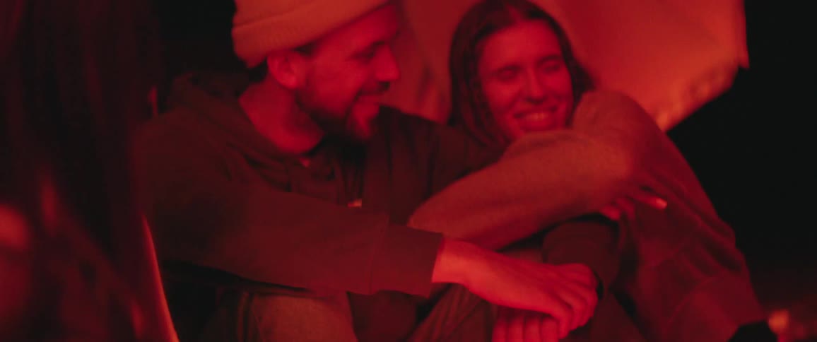 A couple sitting outside at an event while the woman smiles and hugs the mans arm
