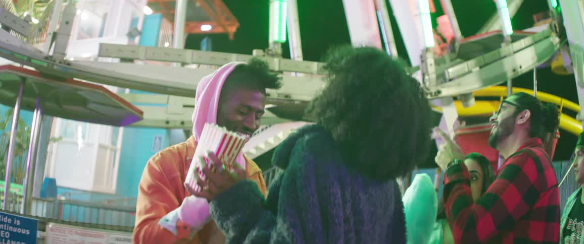 People stand near ferris wheel eating and laughing at night