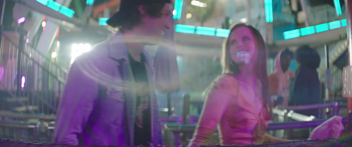 A couple walk and hold hands at a carnival at night