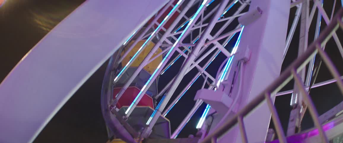 A ferris wheel with colorful cars is moving slowly around with lights flashing in the night sky