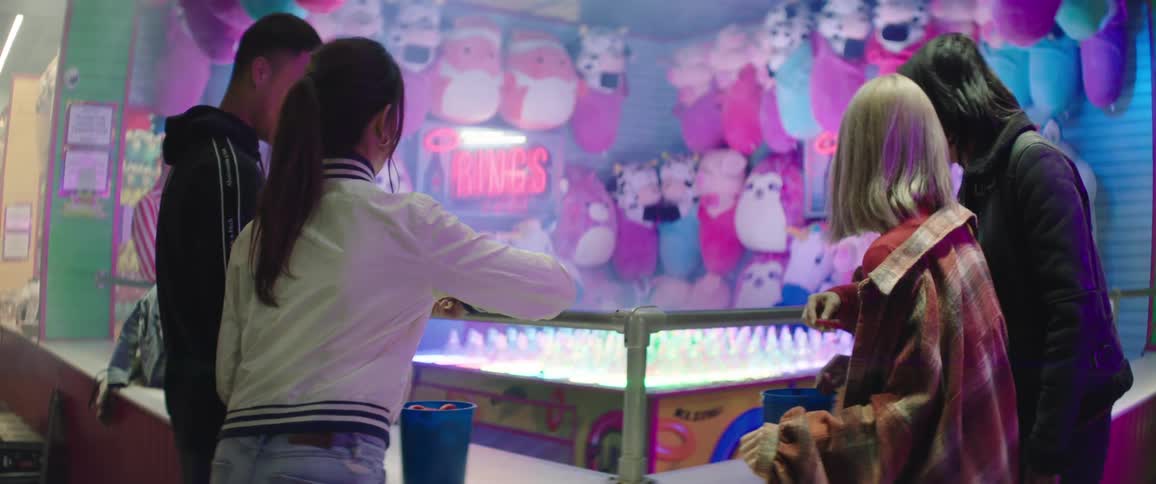 Two men and two women play a ring toss game in a carnival with plush toys in the background