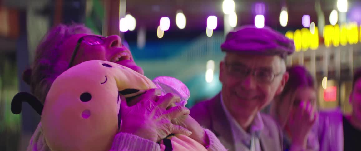 Elderly woman hugs a stuffed bee toy while at a carnival with family