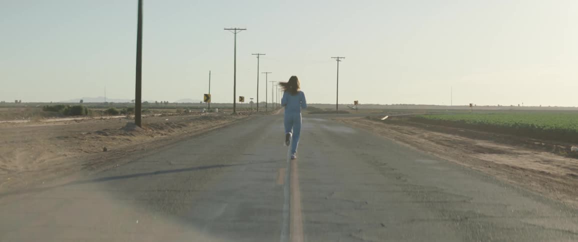 Young long haired woman wearing sports clothes jogging down a road in a rural area at sunset