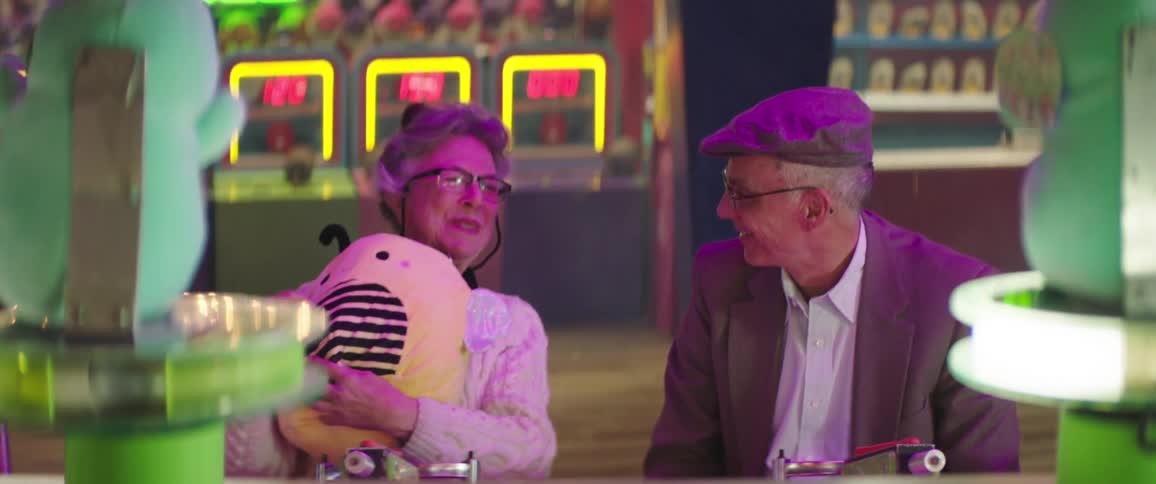 An elderly man hands a stuffed toy that he won at a carnival game to his female companion
