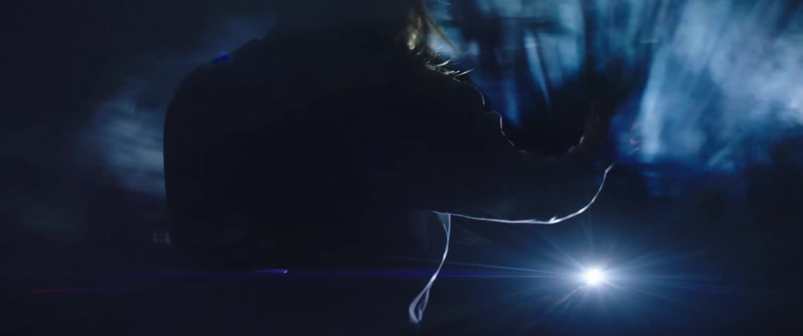 Woman in a dark room with wind blowing her hair and smoke casting over a flare of light