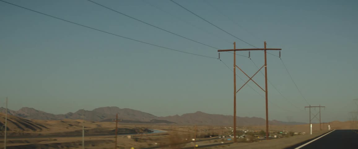 Power lines on the outskirts of a city in a rural area at daytime next to a road
