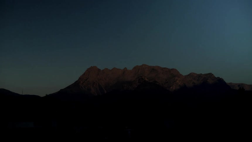 A stony mountain ridge slowly becomes illuminated as the sun rises