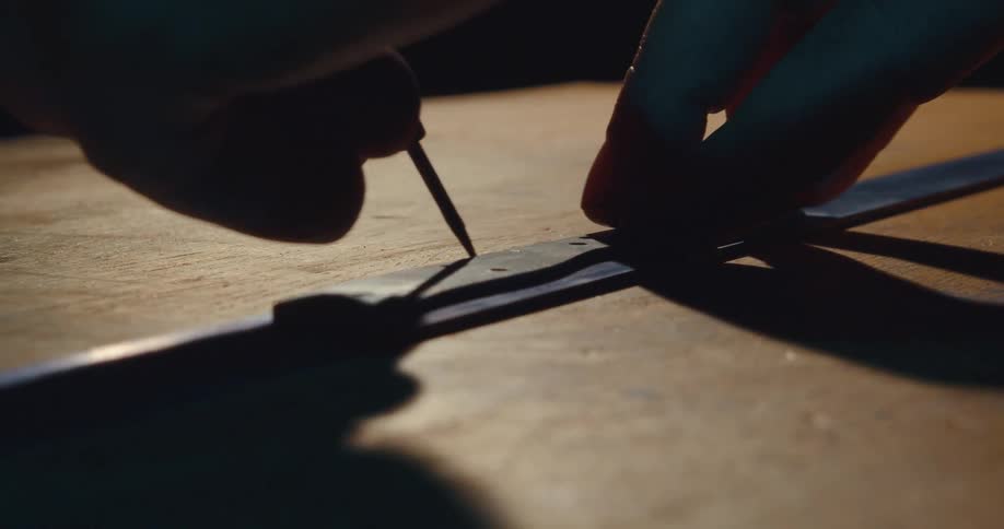 A man draws a line on a wood table with a ruler