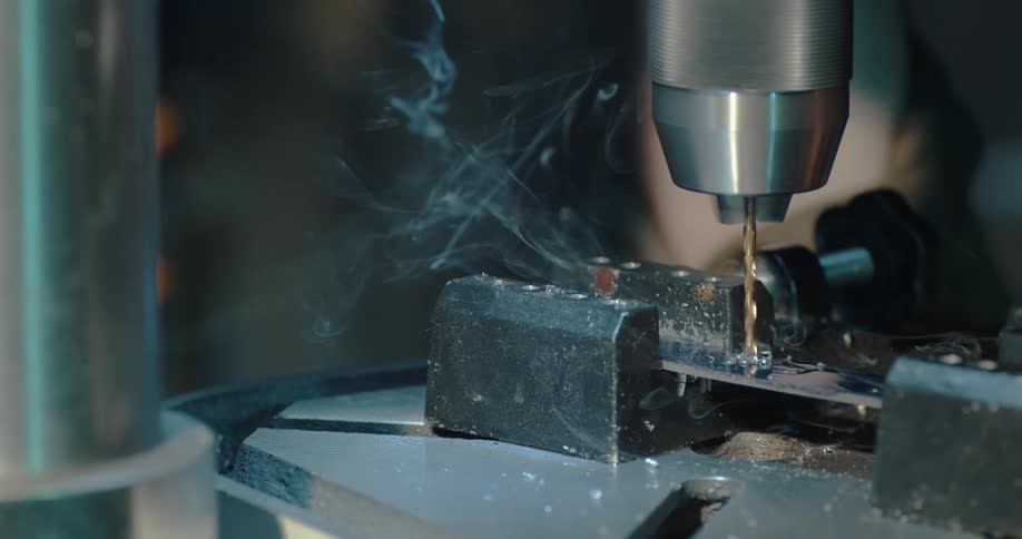 Smoke billows out as a man drills a hole through a piece of metal in his garage