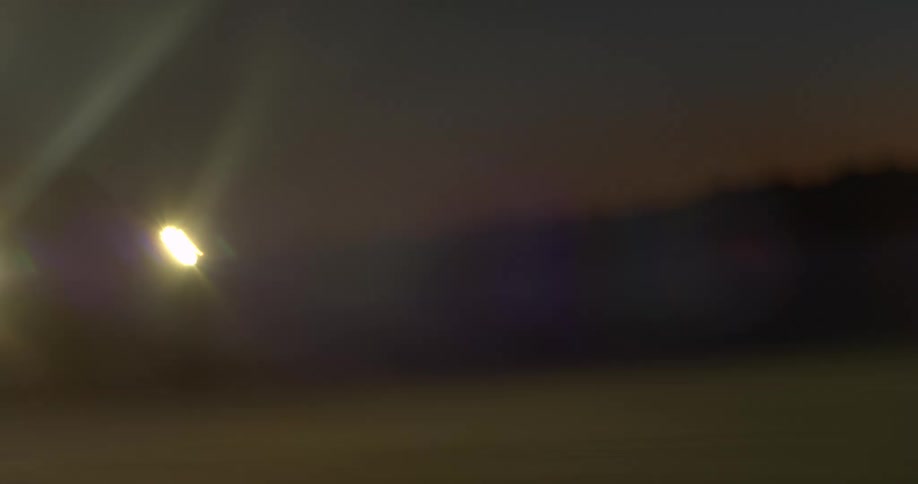 A vehicle driving with its headlights on with a mountain range the sky and clouds in the background