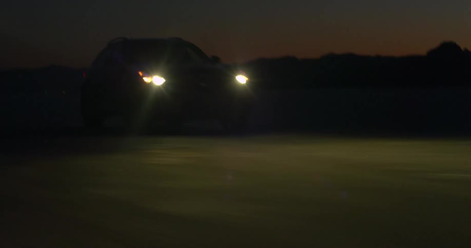 A vehicle driving in the desert with a mountain range the sky and clouds in the background