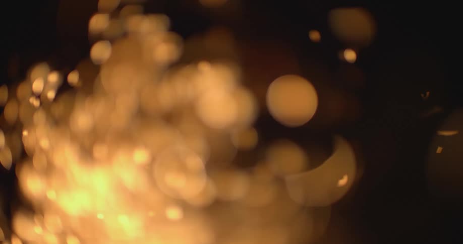 Out of focus close up of a rain of yellow sparks against a dark black background