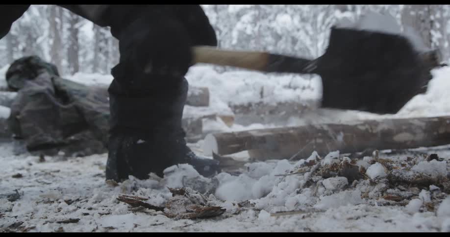 A man digs up snow from where a campfire had been built in a forest