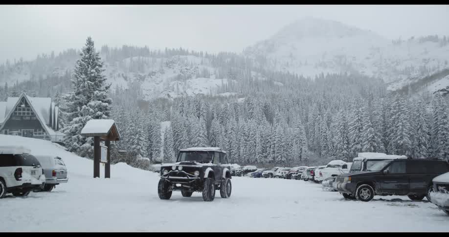 A jeep drives out of the parking of a packed winter resort covered in a blanket of snow