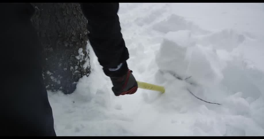 Man in black winter clothes shovels snow with a yellow shovel