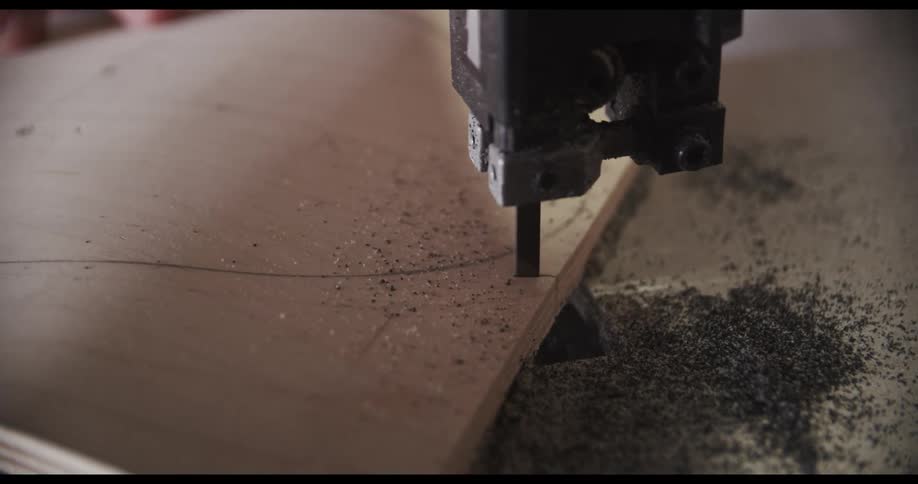 A person moves a thin wooden board to allow a band saw to cut along a traced line
