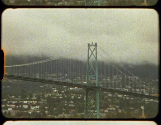 Film of suspension bridge over a river next to a town