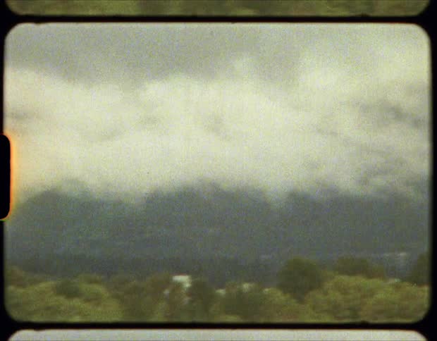 White thick clouds covering the mountain range surrounding a town on film