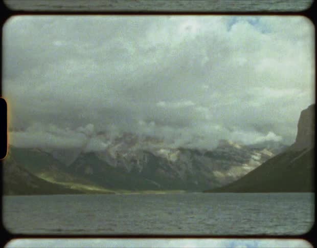 Film of the calm waters of a lake near the cloud covered peaks of a mountain range