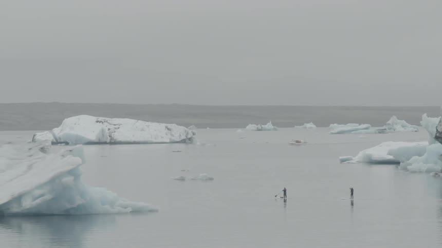 Two people stand on a large, icy body of water