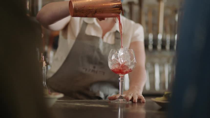 Bartender pouring a red cocktail over ice