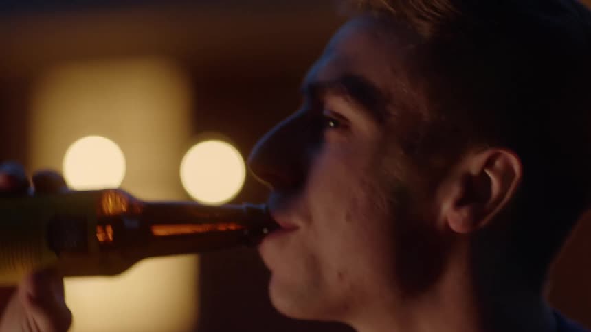 Young male drinking a bottle of beer indoors