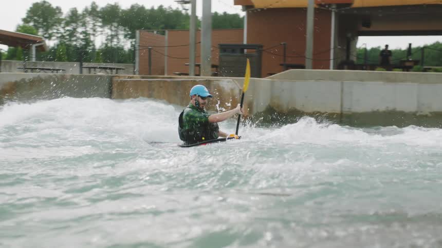 A man with a hat and sunglasses kayaking on a river with a paddle with trees the sky and clouds in the background