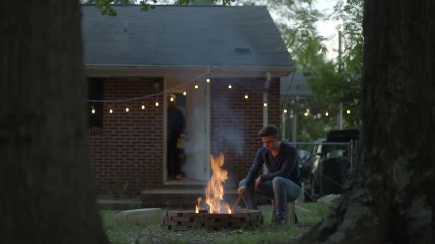 Man tending a bonfire in a backyard