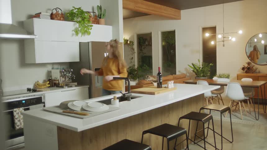 Woman walking into kitchen carrying a wine bottle then getting a wine glass