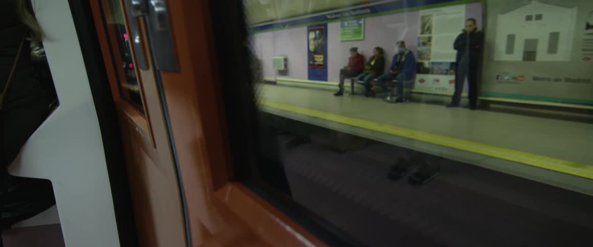 People waiting at a train station as a train full of people drives past