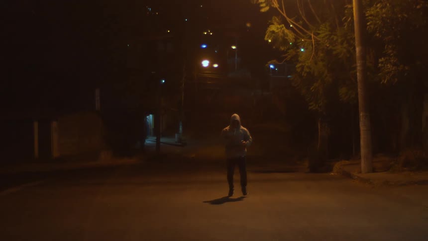 A large man in a hooded jacket runs for exercise along a street at night