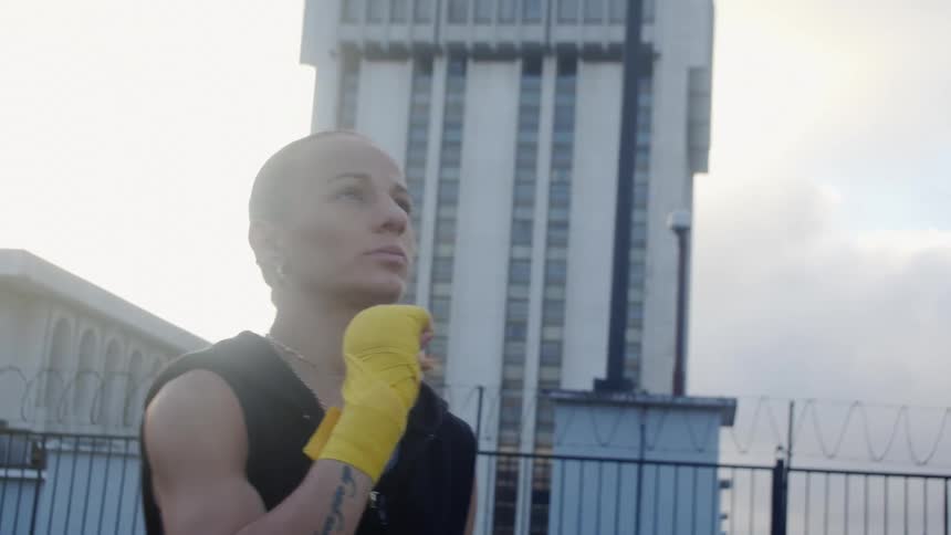 A woman on a rooftop kisses her hand before boxing