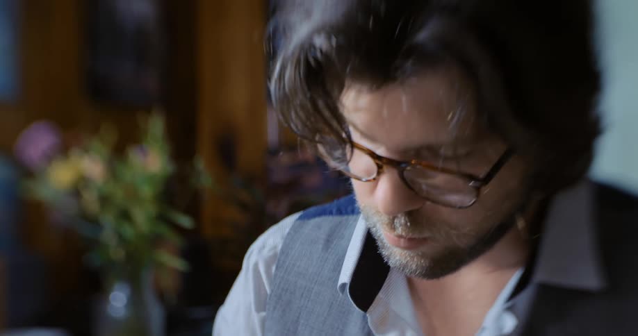 Man with eyeglasses indoors at home looking down and moving his arm