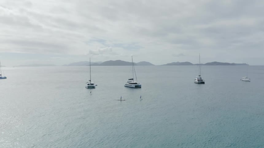 Boats parked out in the middle of the ocean while people row around on boards