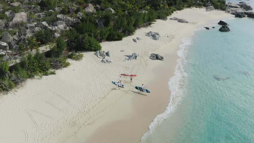 Three people on a beach get their paddleboards ready to take in the water