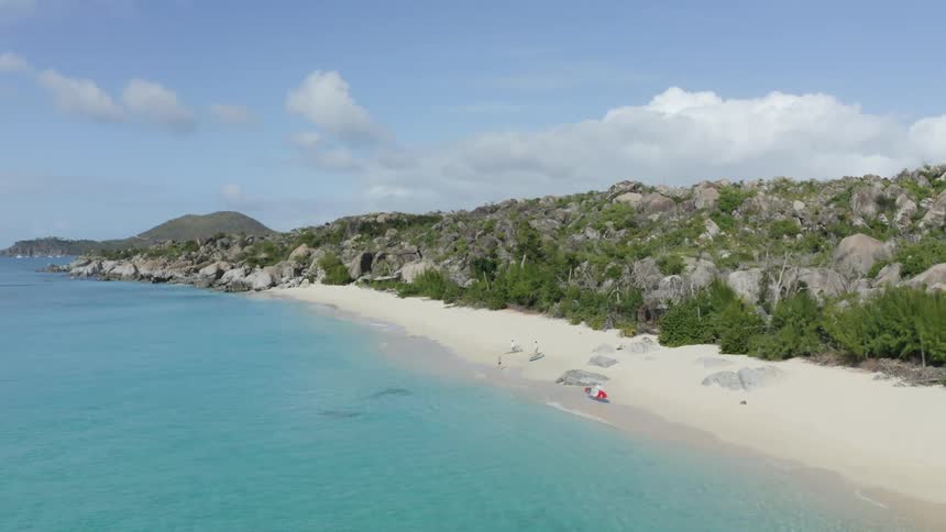 Aerial of people with paddleboards walking along shoreline on white sandy beach