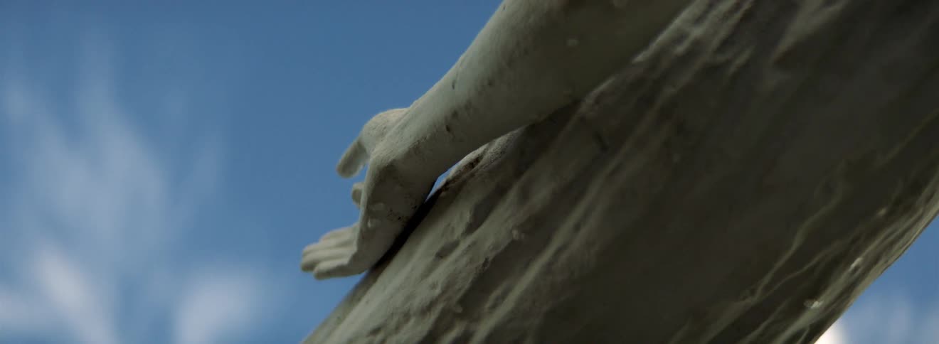 A statue of the lord jesus christ with his hand nailed to the cross with the sky and clouds above