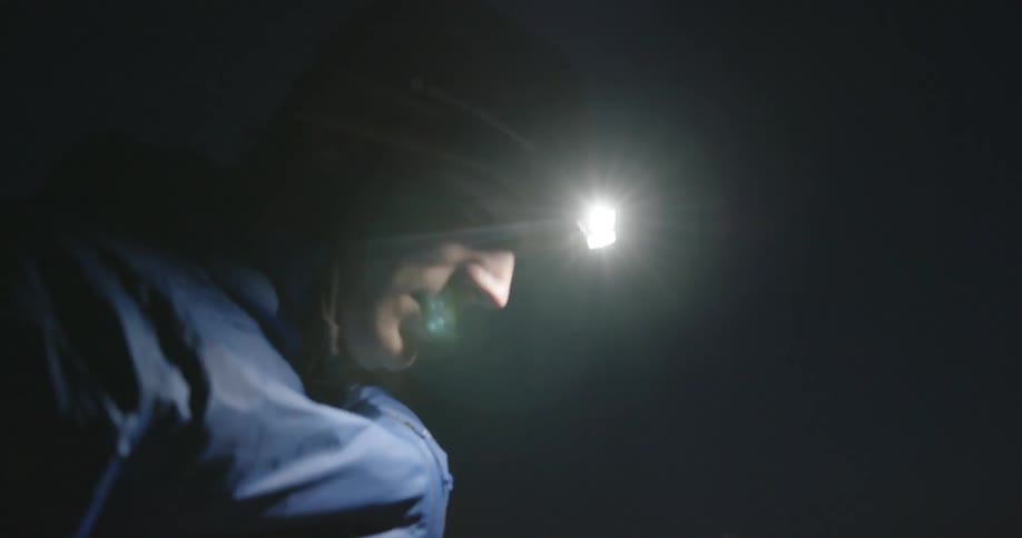 Man wearing a head lamp looks for something in the floor in a field at night