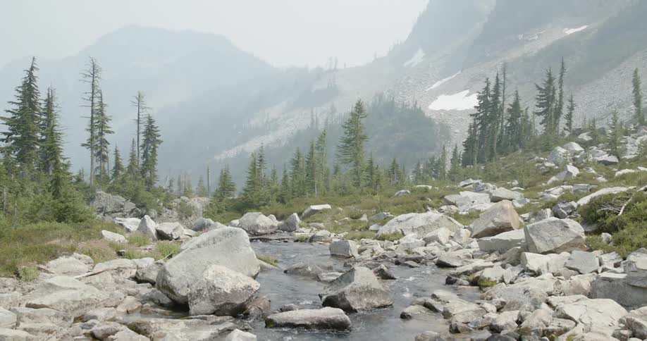 A stream of water flows down a sloping mountain through rocky terrain